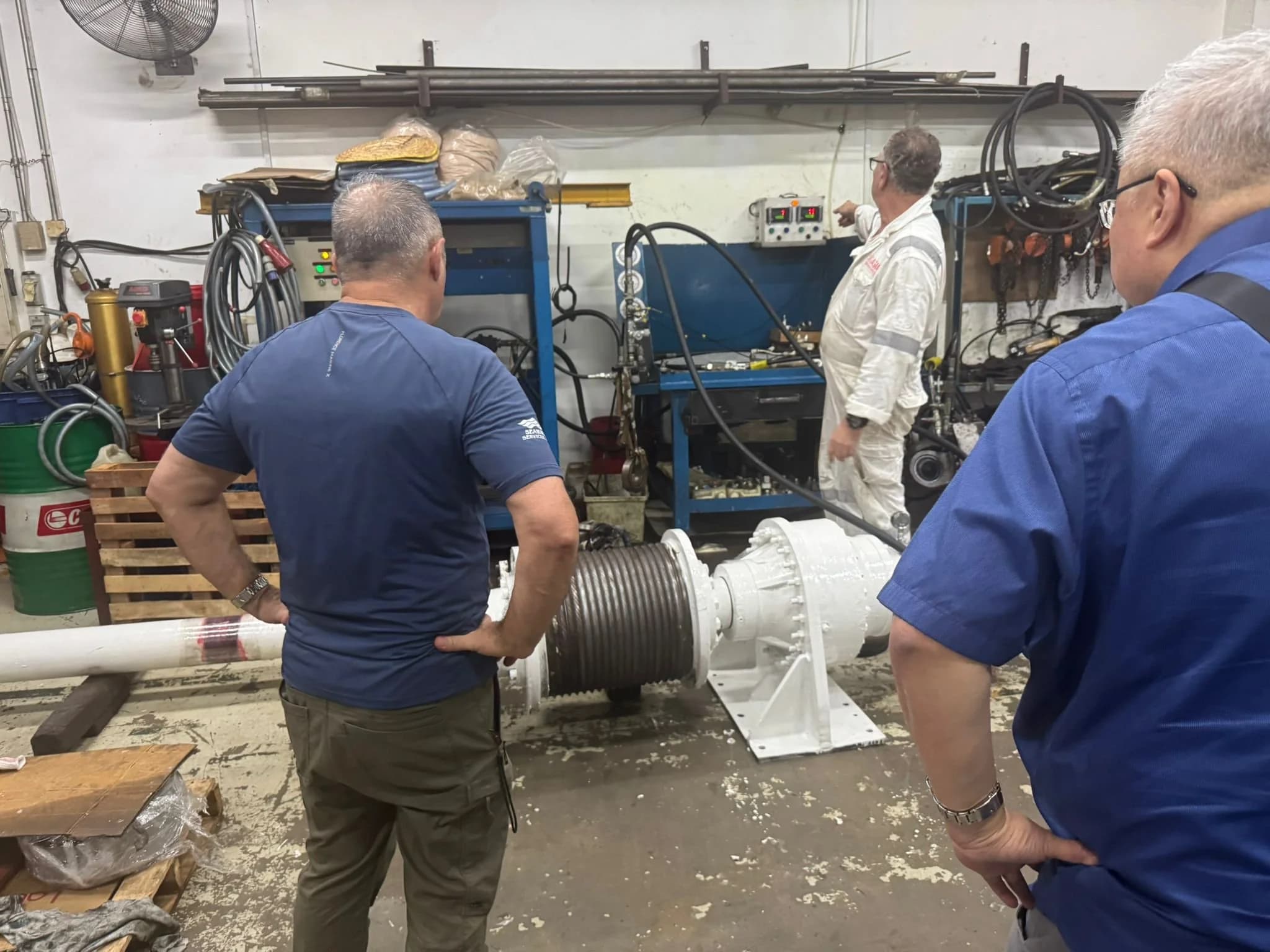 Technicians inspecting an overhauled winch on the workshop floor